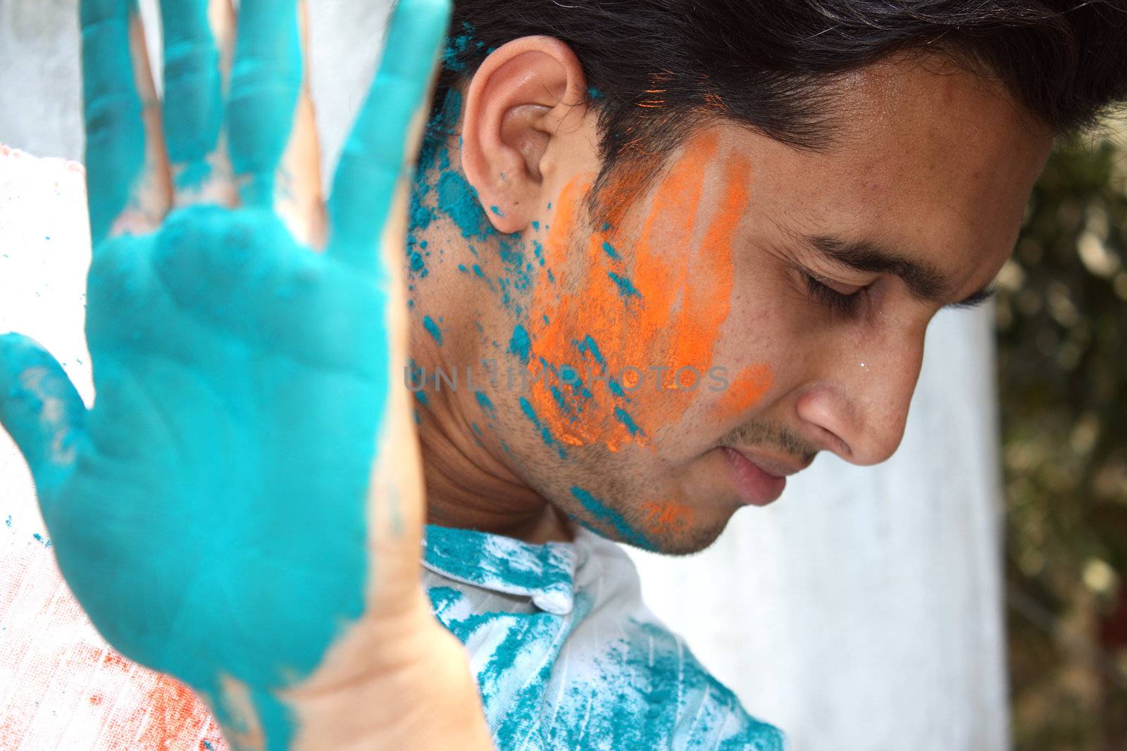 A young Indian man uses his hand to stop holi colors getting on to his face.