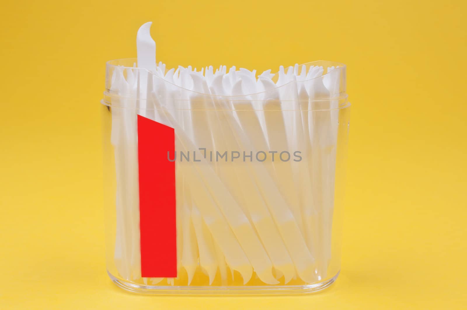 Toothpicks in clear plastic container on yellow background