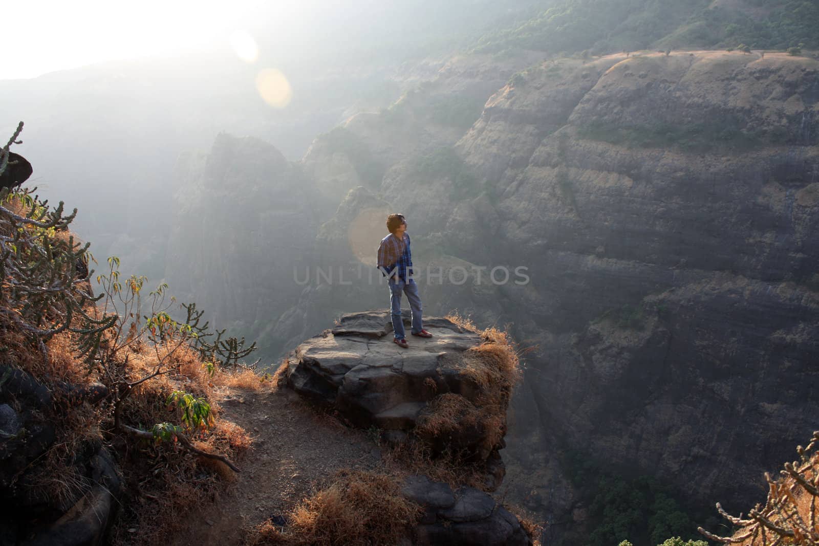A young Indian guy contemplating on a rock near a valley.