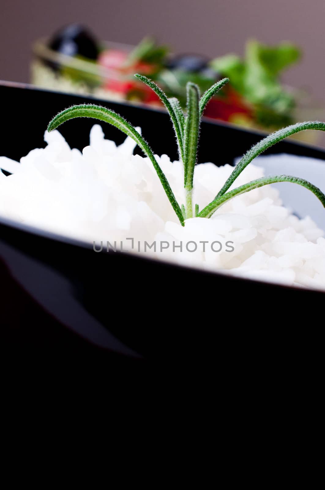 White rice in black bowl on salad background