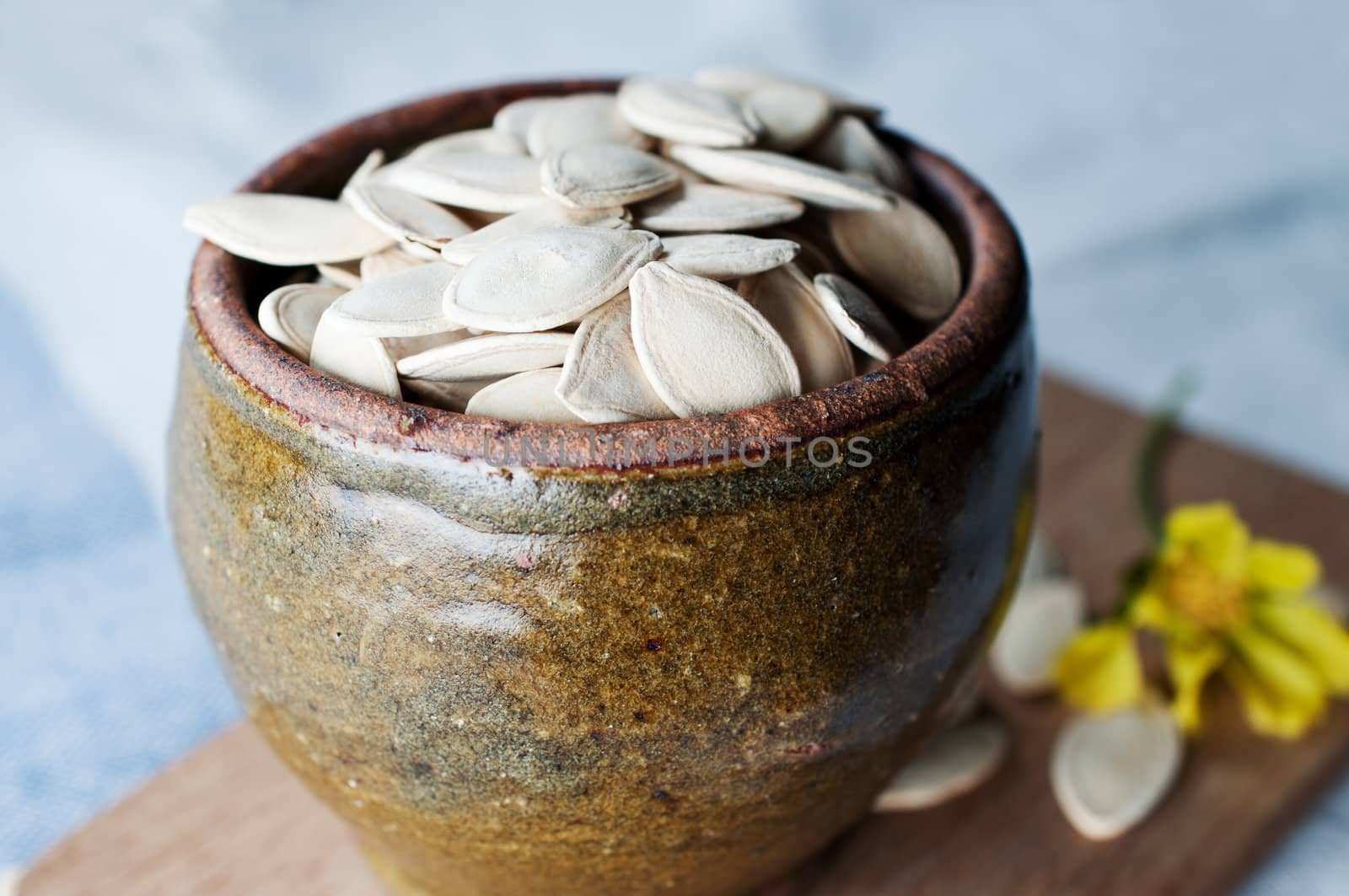 Ceramic bowl full of pumpkin seeds on kitchen table  by Nanisimova
