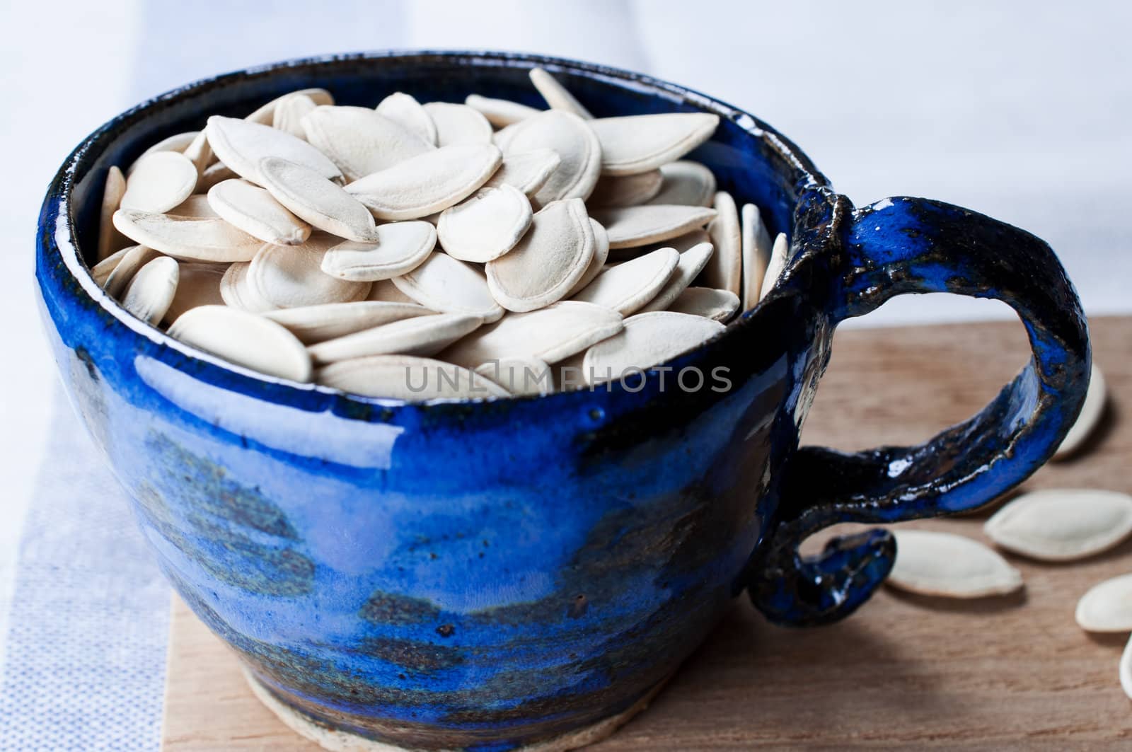 Pumpkin seeds in cup on wooden board by Nanisimova