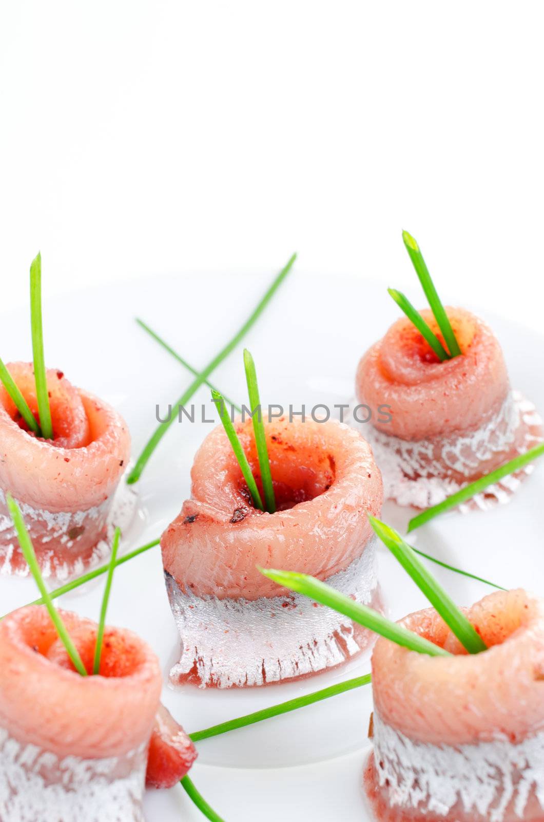 Rolls of marinated herring close up with spring onion on a plate