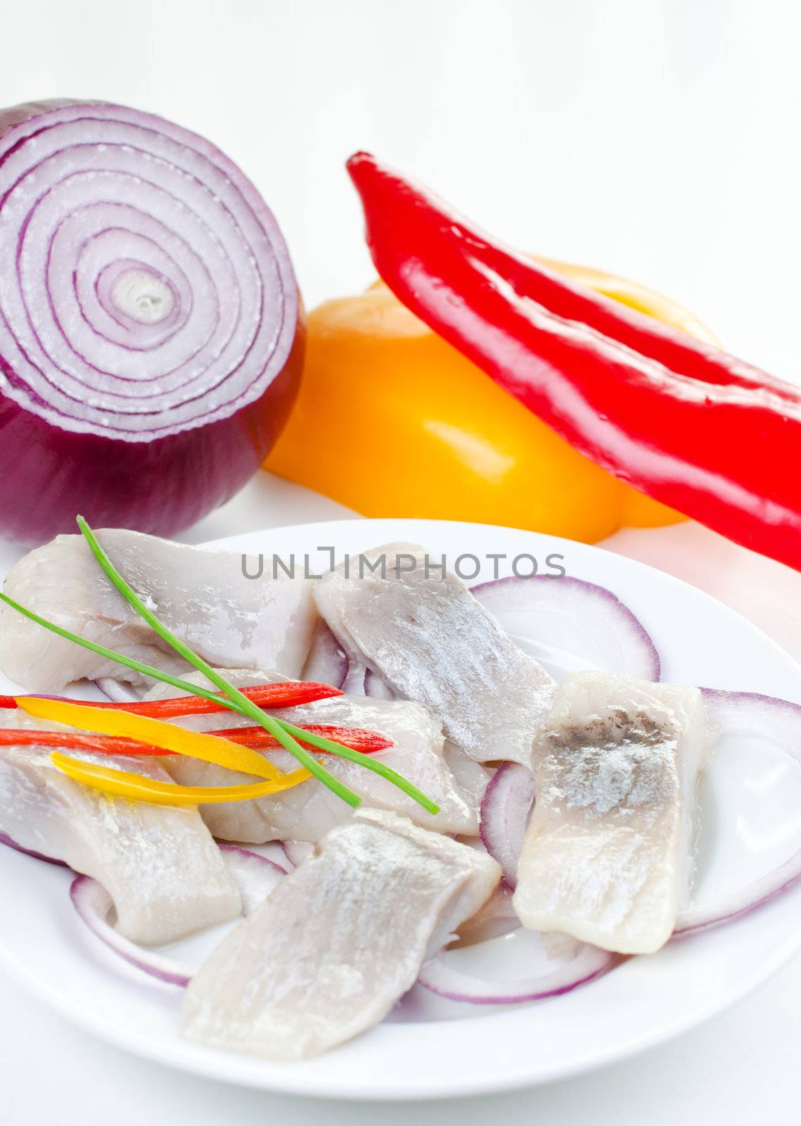 Marinated herring bites on a plate with onion and red and yellow pepper