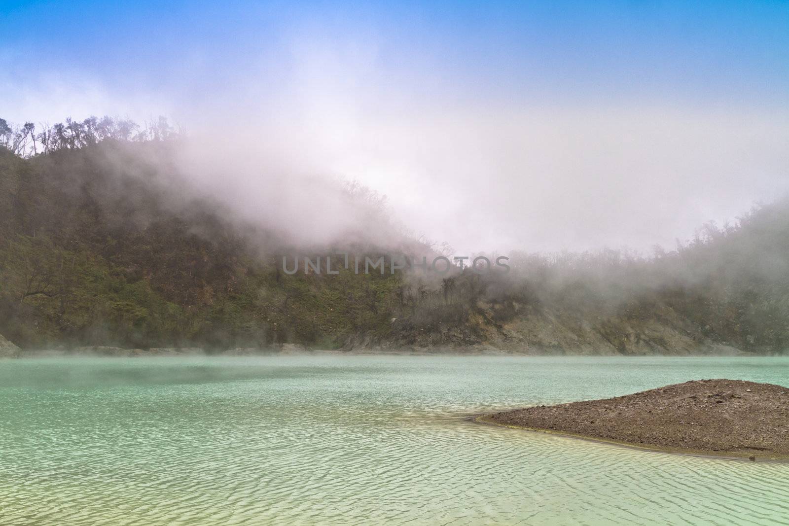 Green Volcanic crater lake with fog forming against blue sky in Ciwidey, West Jawa