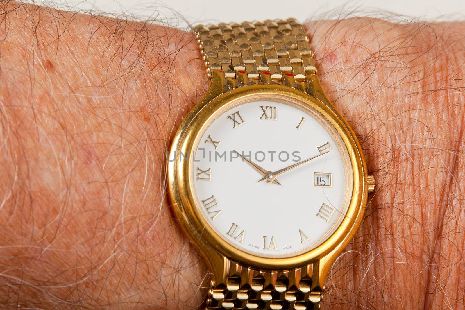 Gold watch and band in close up on wrist of hairy senior man