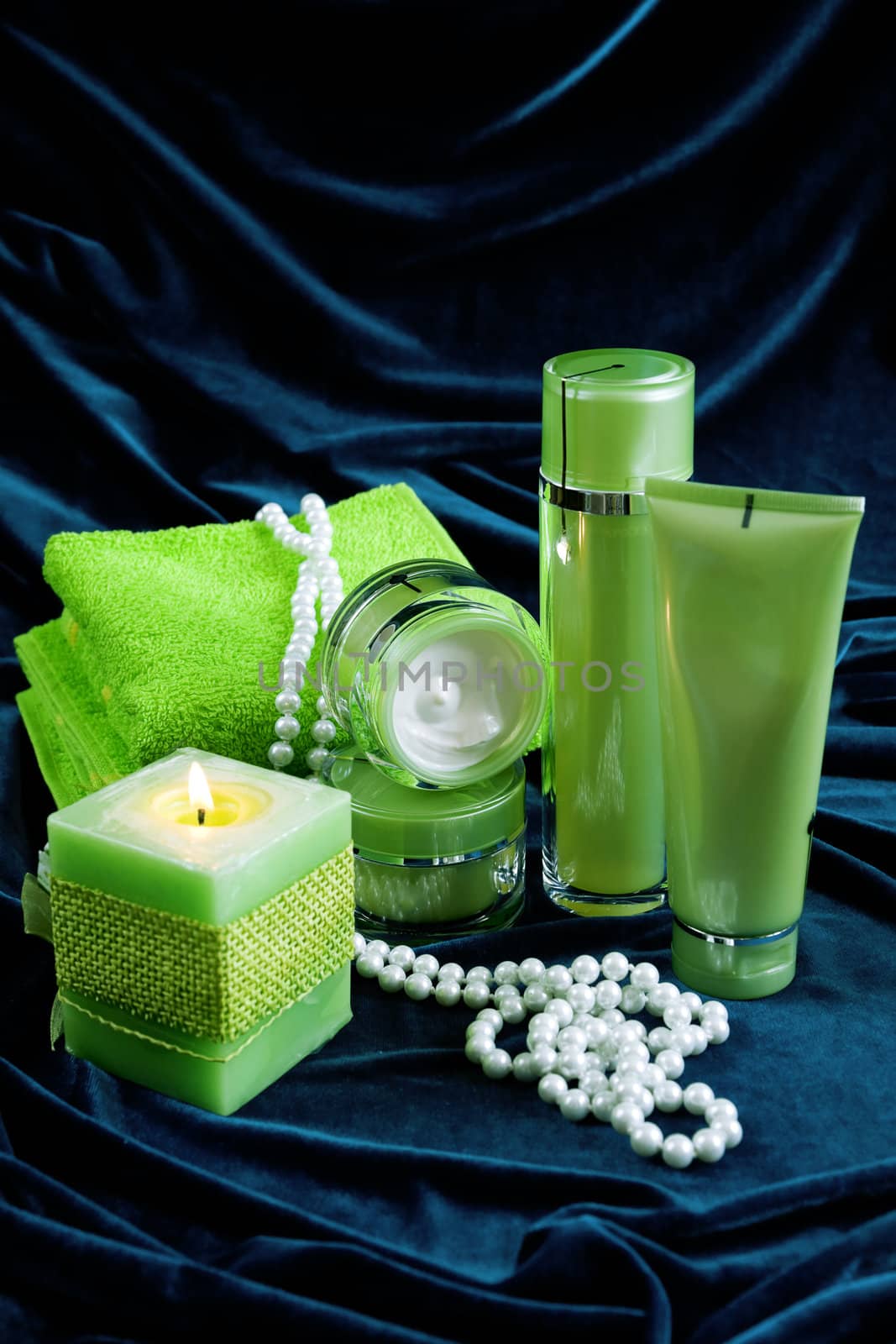 Creams for body care, candles and a green towel on a dark blue glossy velvet