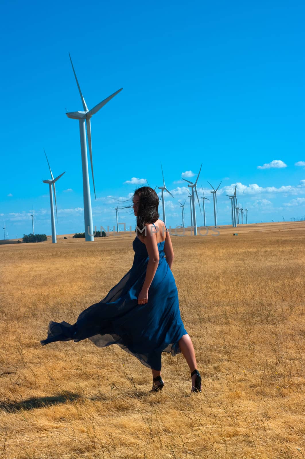 Girl with a designer silk dress on a farm near the wind turbines. 


