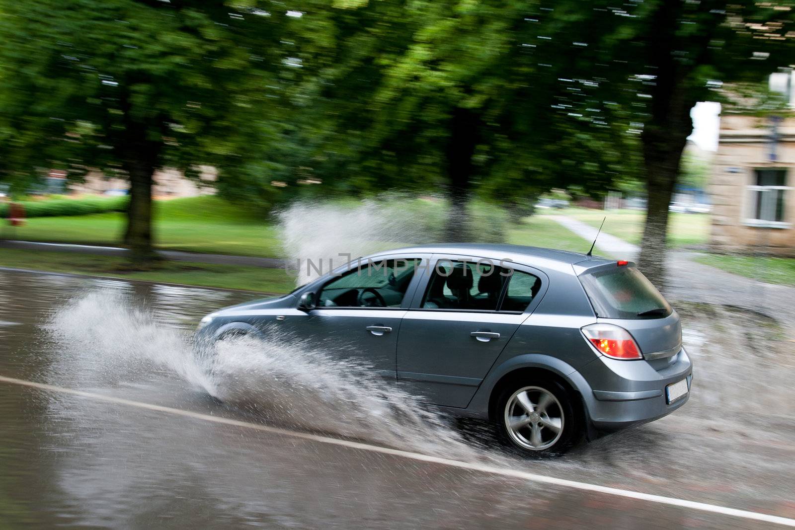 A car splashes through a large puddle on a wet road.