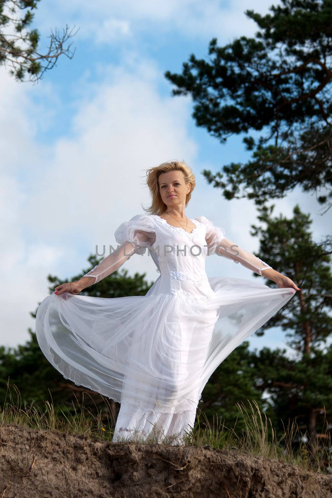 Woman stands near precipice. Wind blows the white dress.