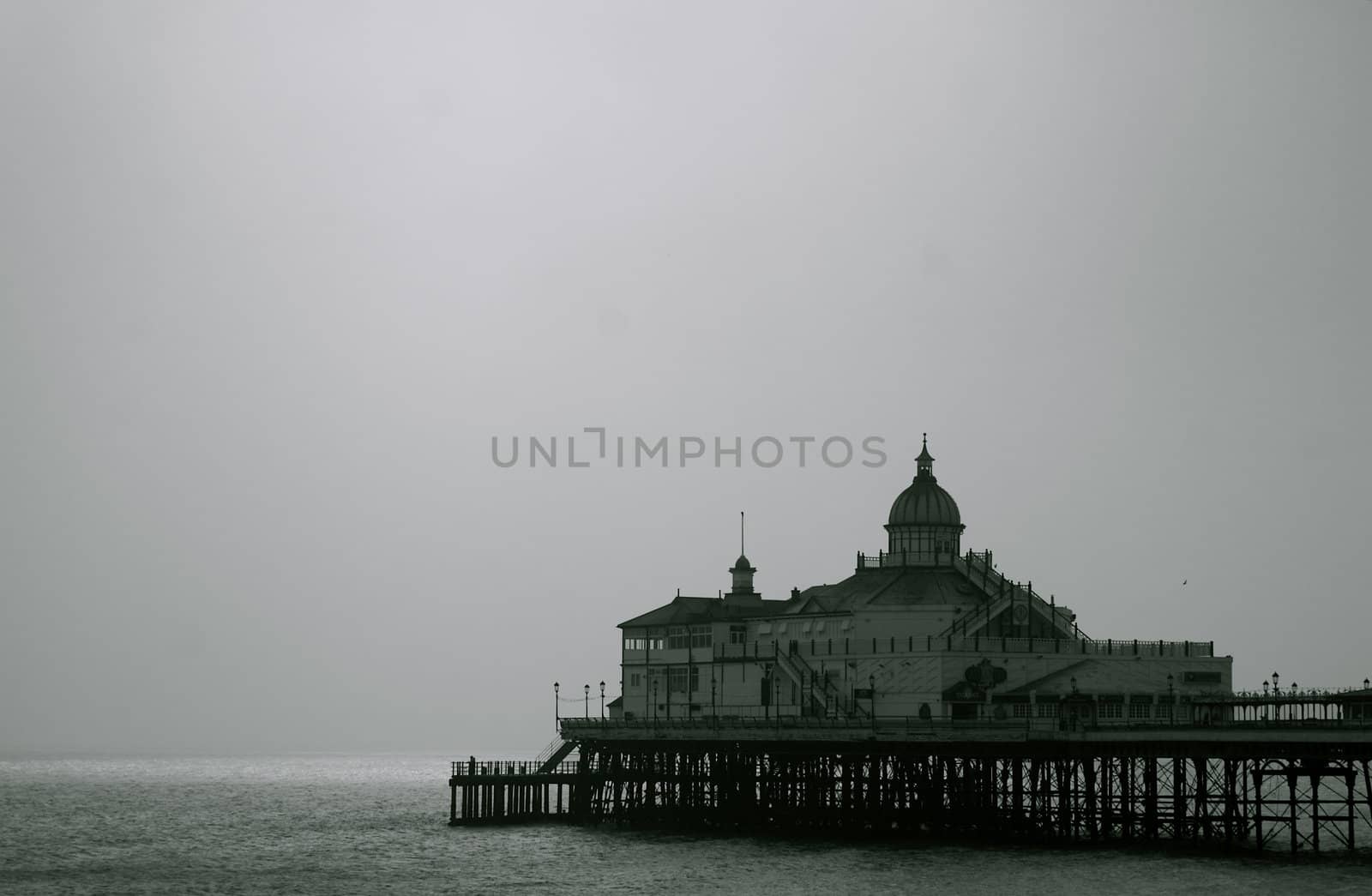 Long, old fashioned and ornate English seaside pier at Eastbourne, Sussex against a misty sky and dark grey ocean/ sea, with copy space.