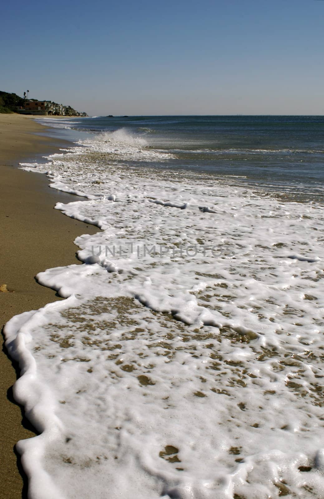 Long foamy wave rolling up on a sandy beach with a blue sky in the horizon, with copy space.