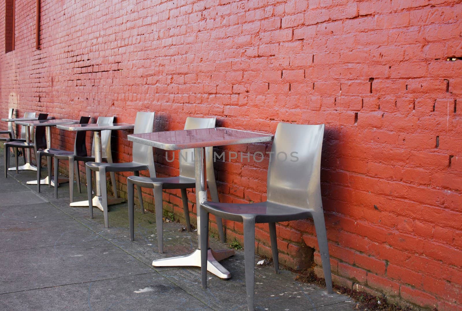 Brushed aluminum tables and chairs on a sidwalk against a red brick wall