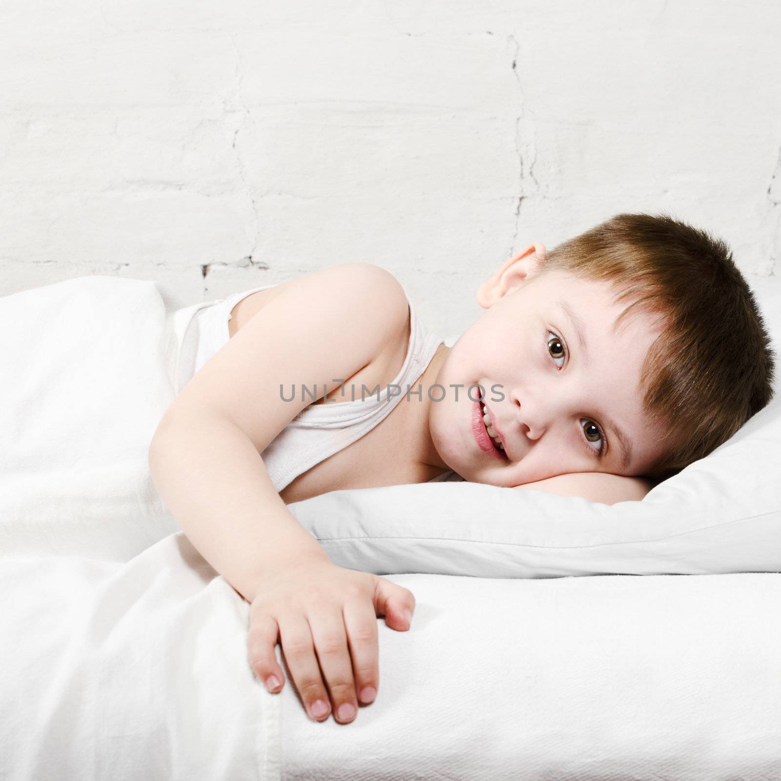 Small toddler boy (4 years old) is lying in bed and smiling. He is looking at the camera