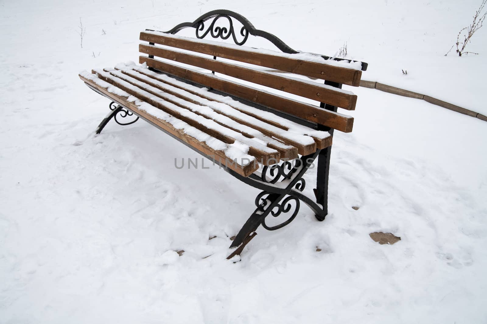 Lonely snow covered bench in city park in winter day
