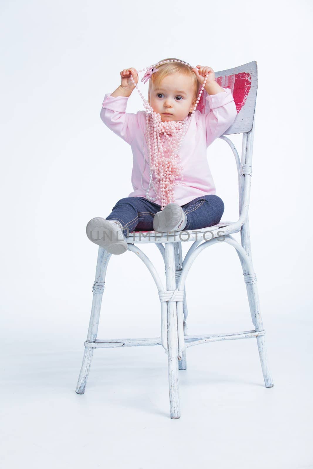 Portrait of an adorable baby girl wearing a pink with pearl necklace sitting on a c