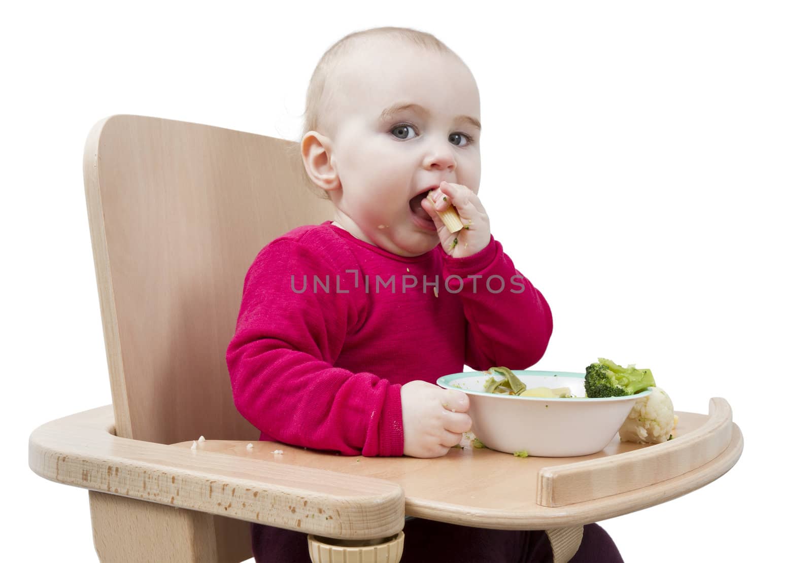 young child in red shirt eating vegetables in wooden chair.