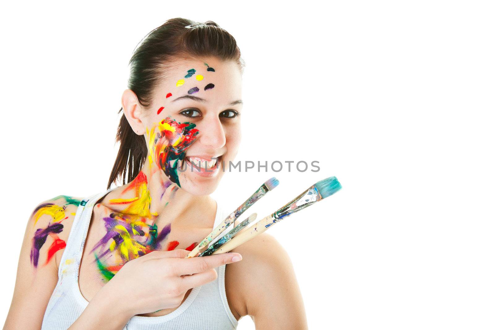 A young, smiling artist with brushes and acrylic paint on her face and body.  Shot on white background.