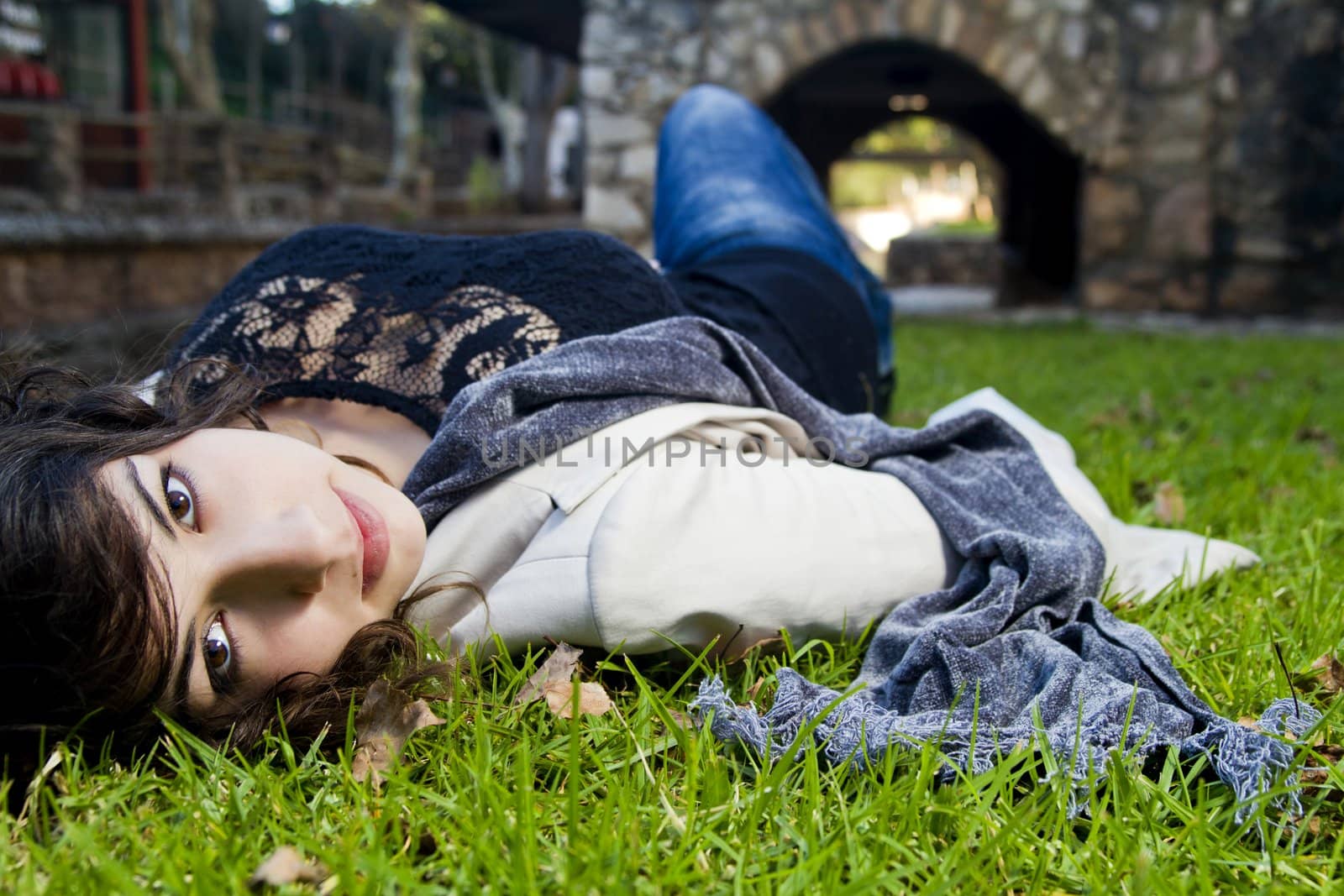 Beautiful young girl lies down on the green grass on a urban park.