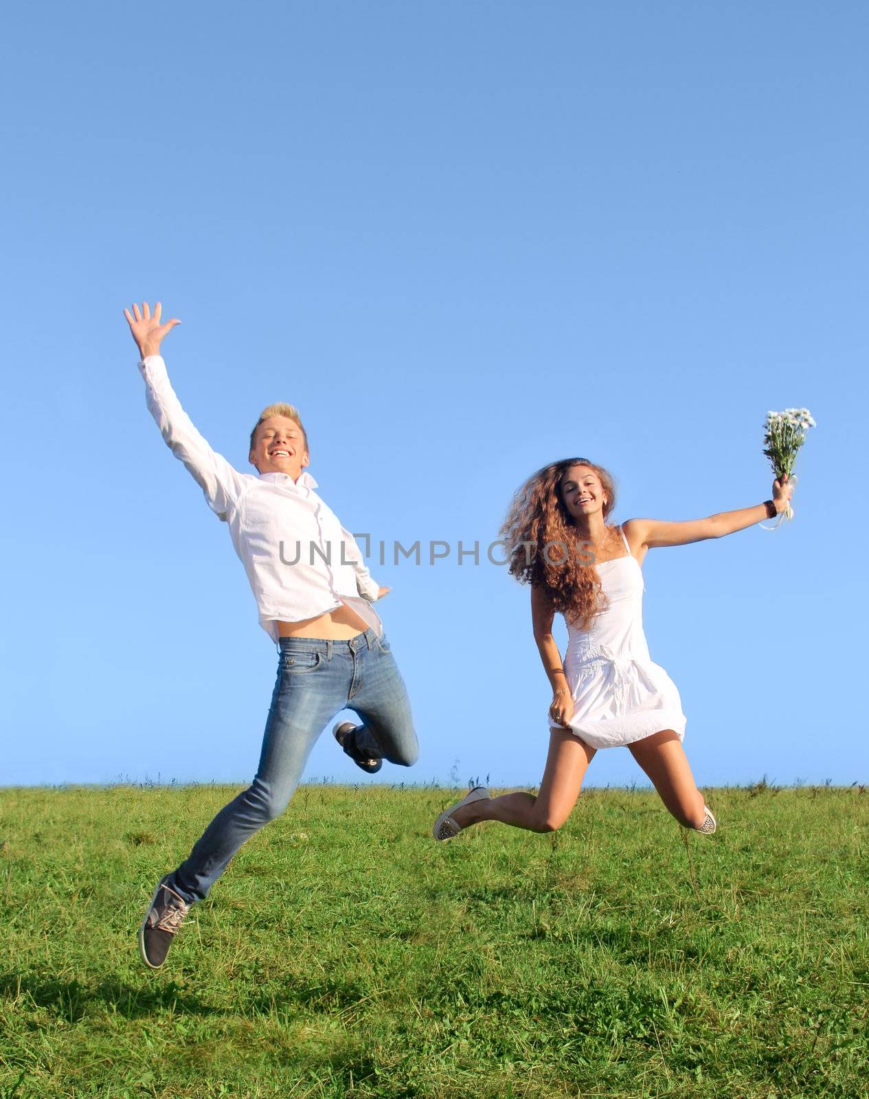 Young happy couple jumping on summer green field