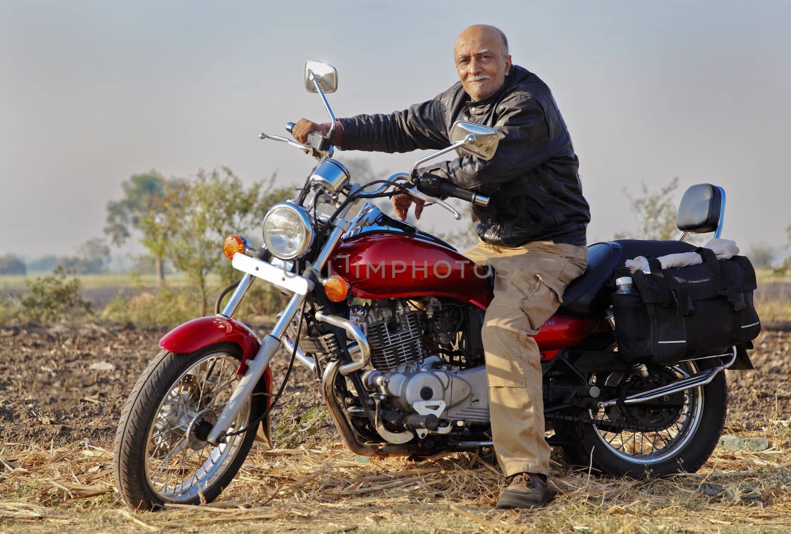 Gujarat India in a rural farmland senior male adult on his red cruiser motorcycle