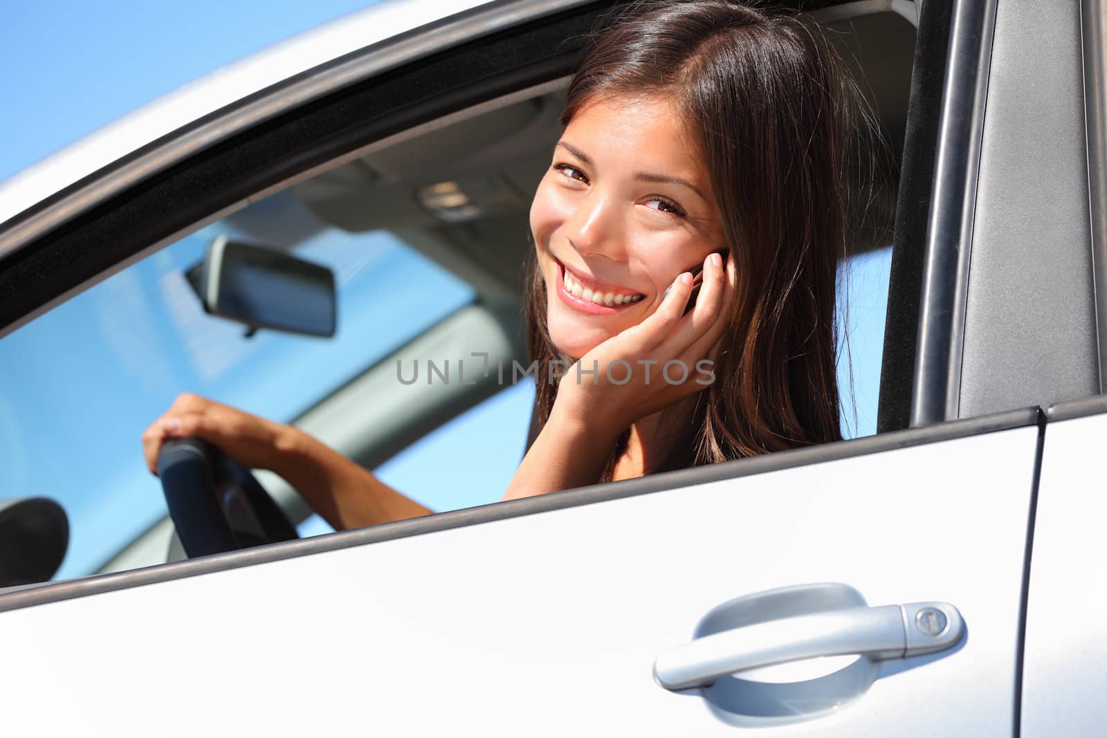 Car woman using smart phone while driving in car. Beautiful young woman talking on mobile phone smiling happy looking at camera. Mixed race eurasian woman.