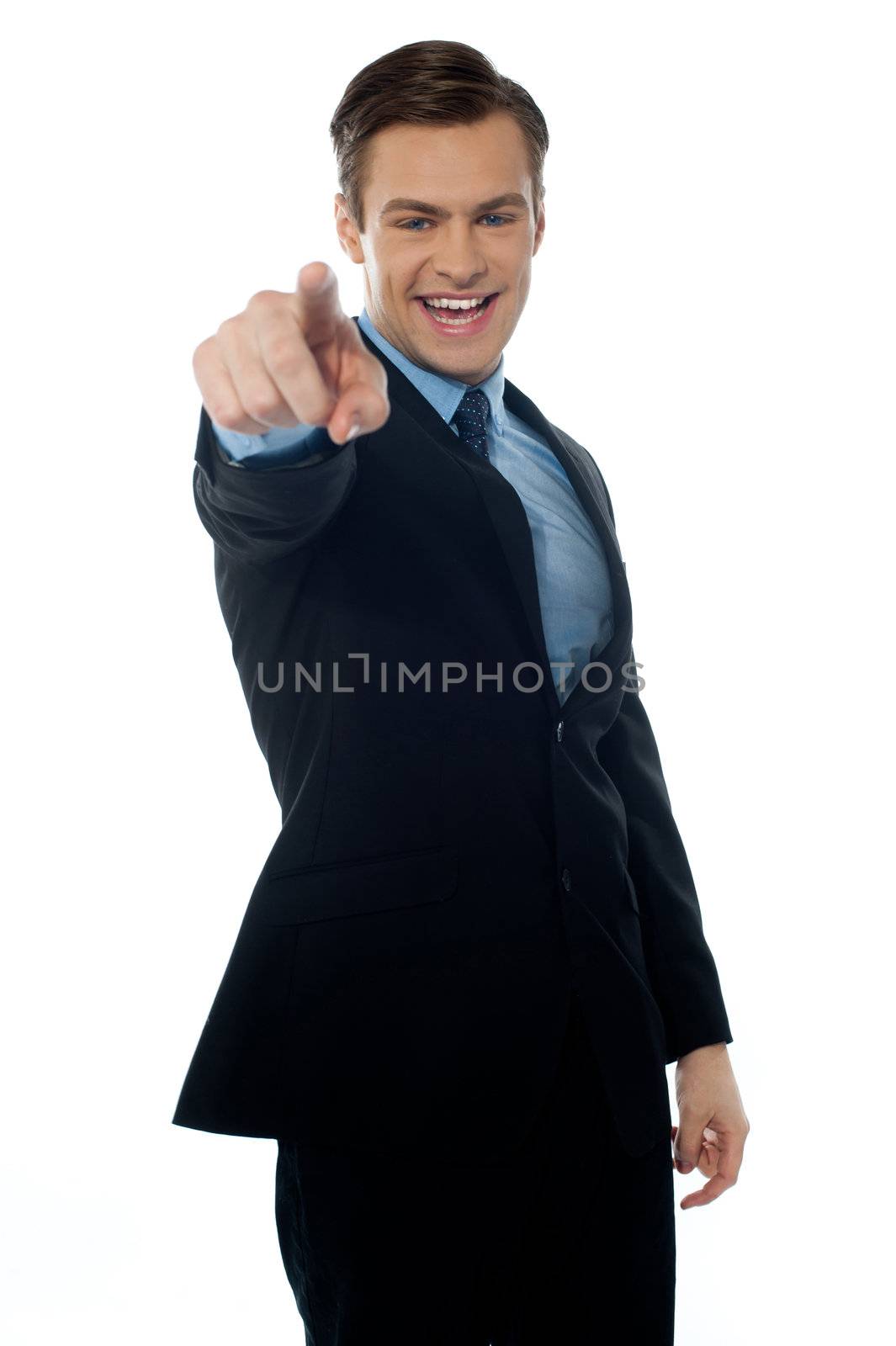Smiling young executive pointing at you in black suit on white background