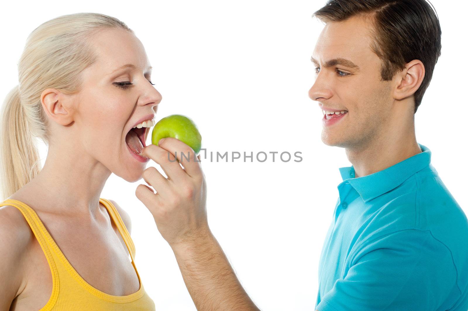 Young guy making her pretty girlfriend eat an apple. Healthy couple