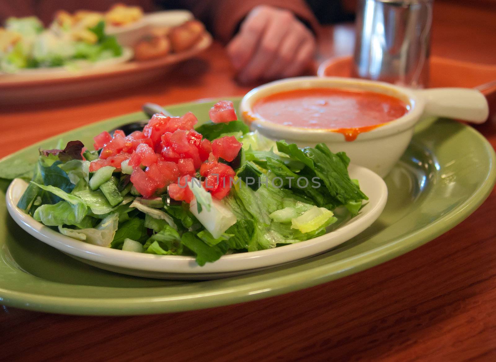 A simple restaurant salad of lettuce, tomato and cucumber with a small bowl of tomato basil soup.