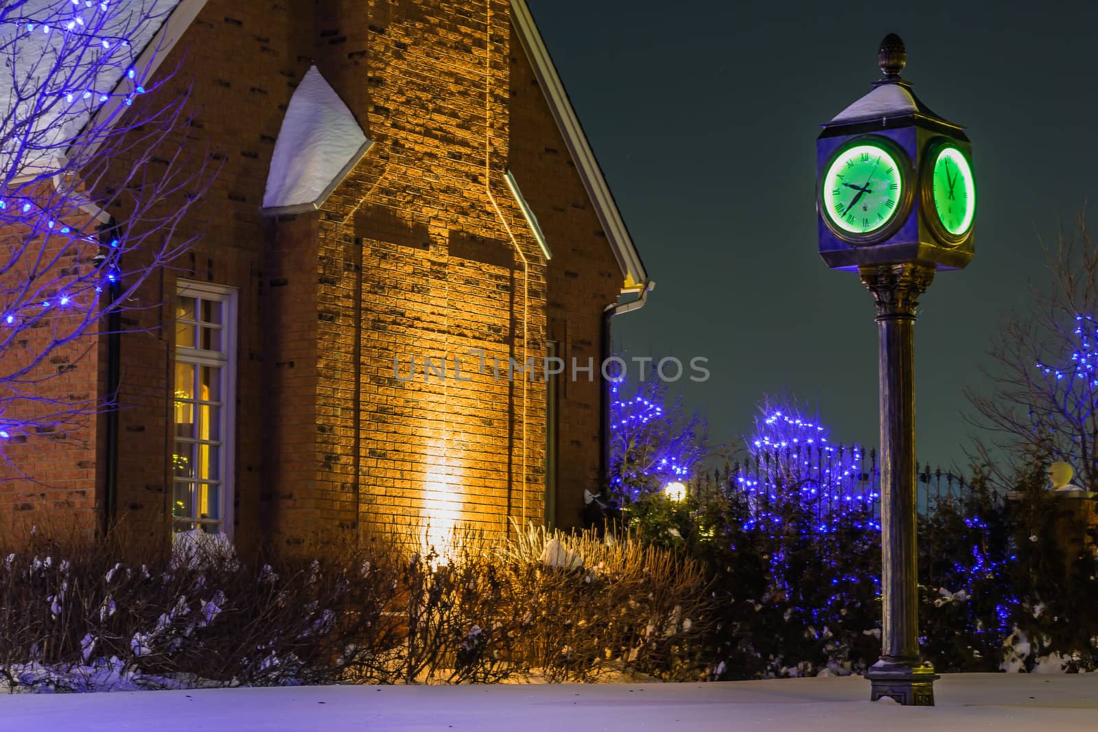 A beautiful old style green clock in the street in front of a big house in a cold winter night in Quebec, Canada