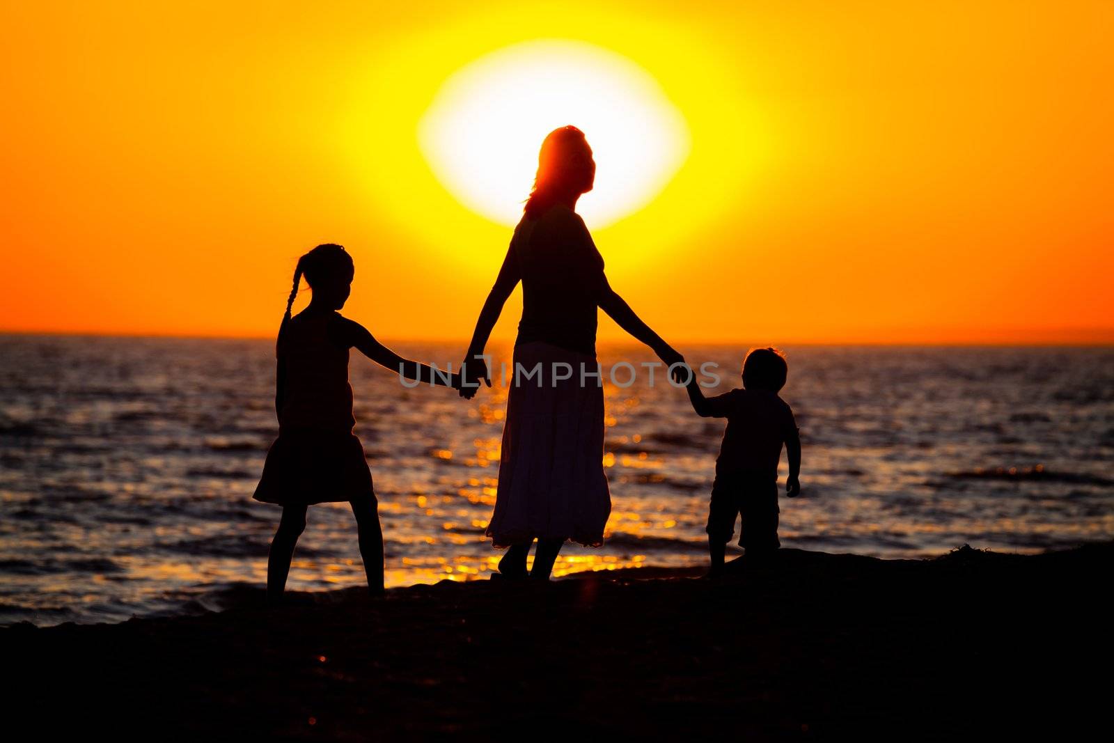 Mother and her kids silhouettes on beach at sunset