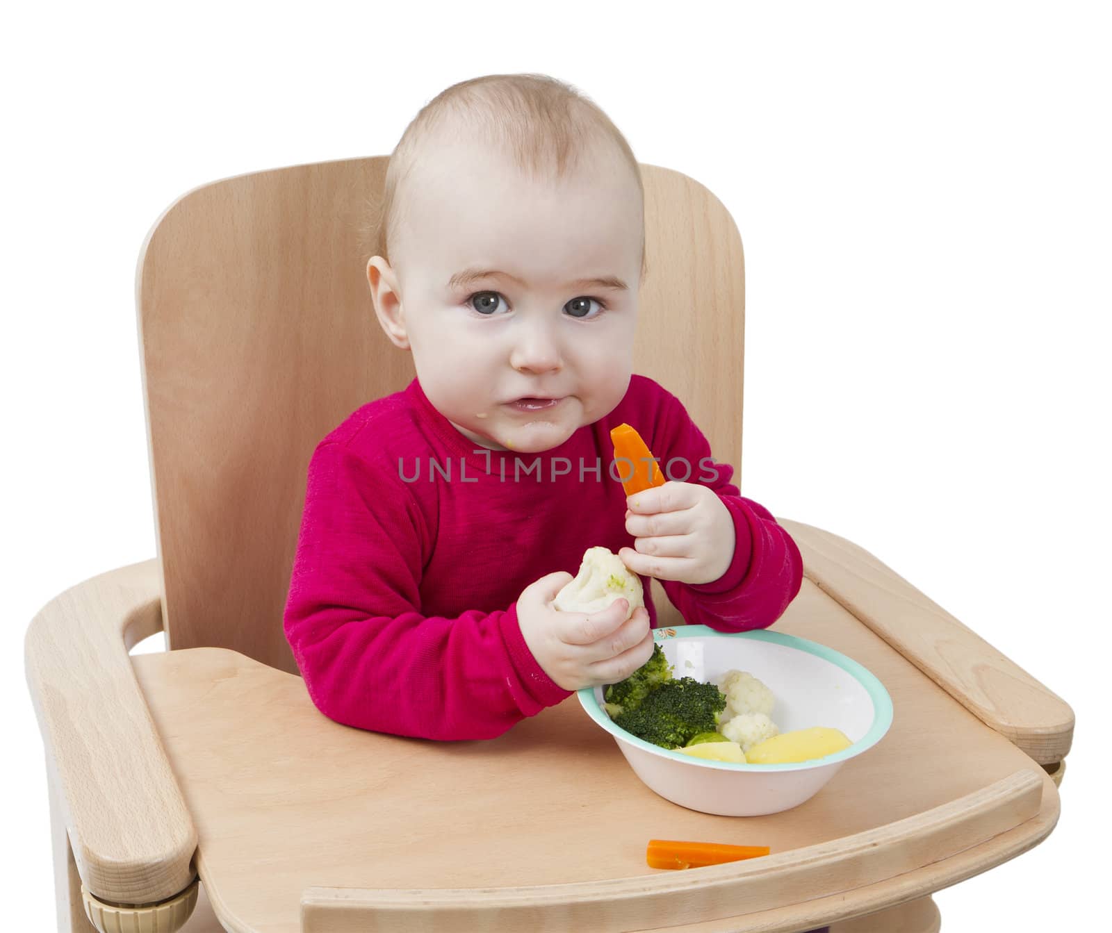 young child in red shirt eating vegetables in wooden chair.