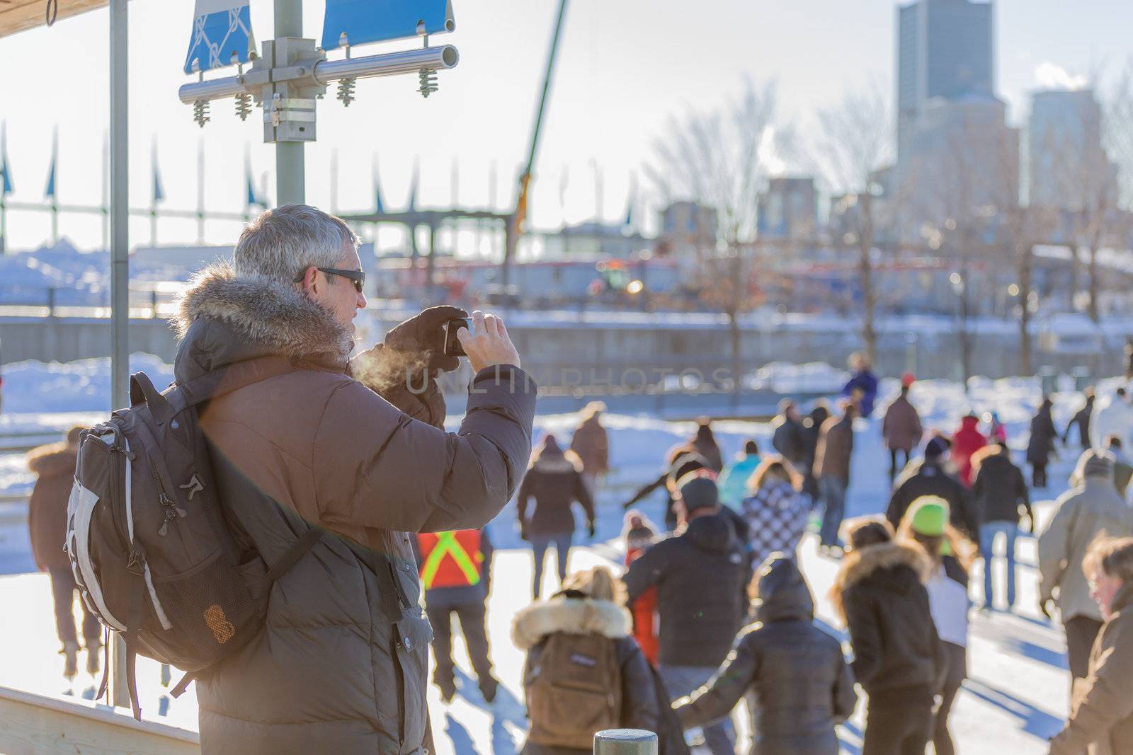 A man taking a picture with her phone in a cold winter day of the Skating Rink in Old Port of Montreal. Quebec, Canada