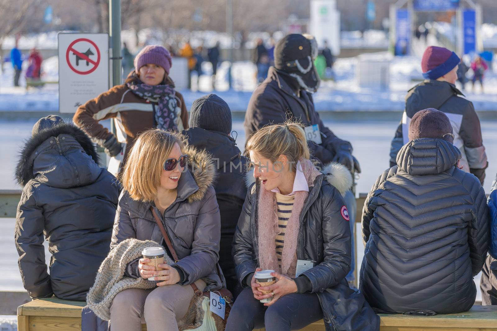  Two women are talking with other and are laughing, while waiting for the Skating Rink to open in the Old Port of Montreal, Quebec, Canada