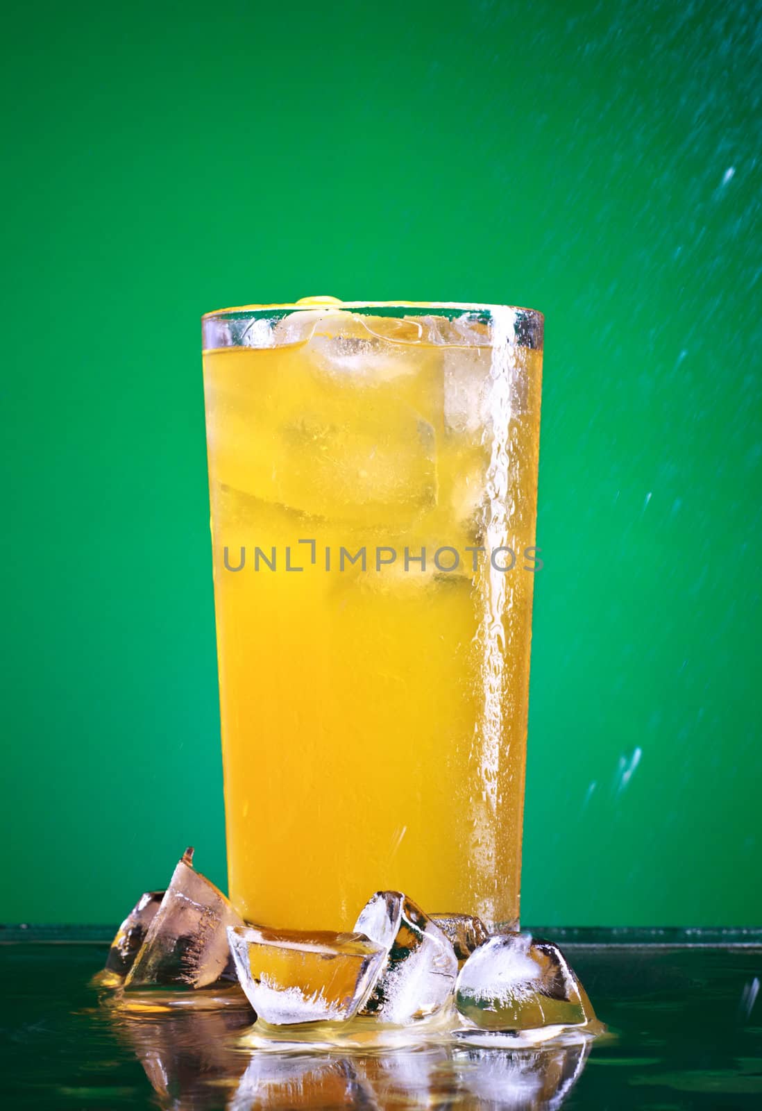 glass of orange soda with ice over green background