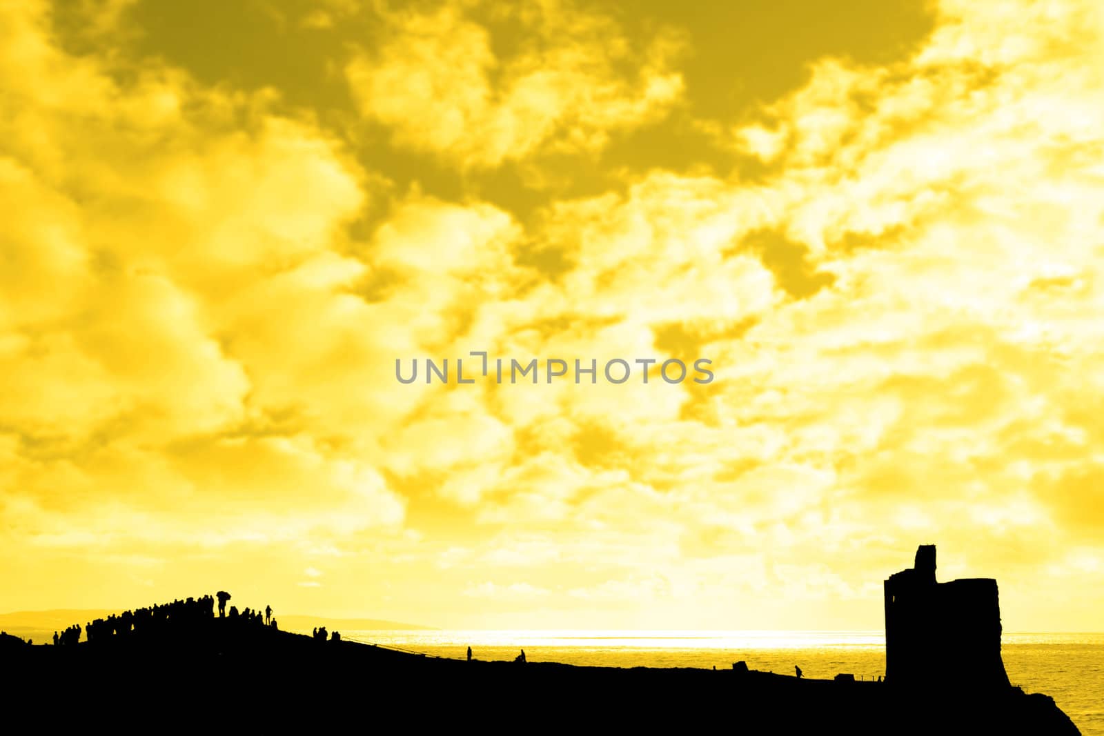 a silhouette of a crowd on a hill beside old castle with a view of the sea and sunset