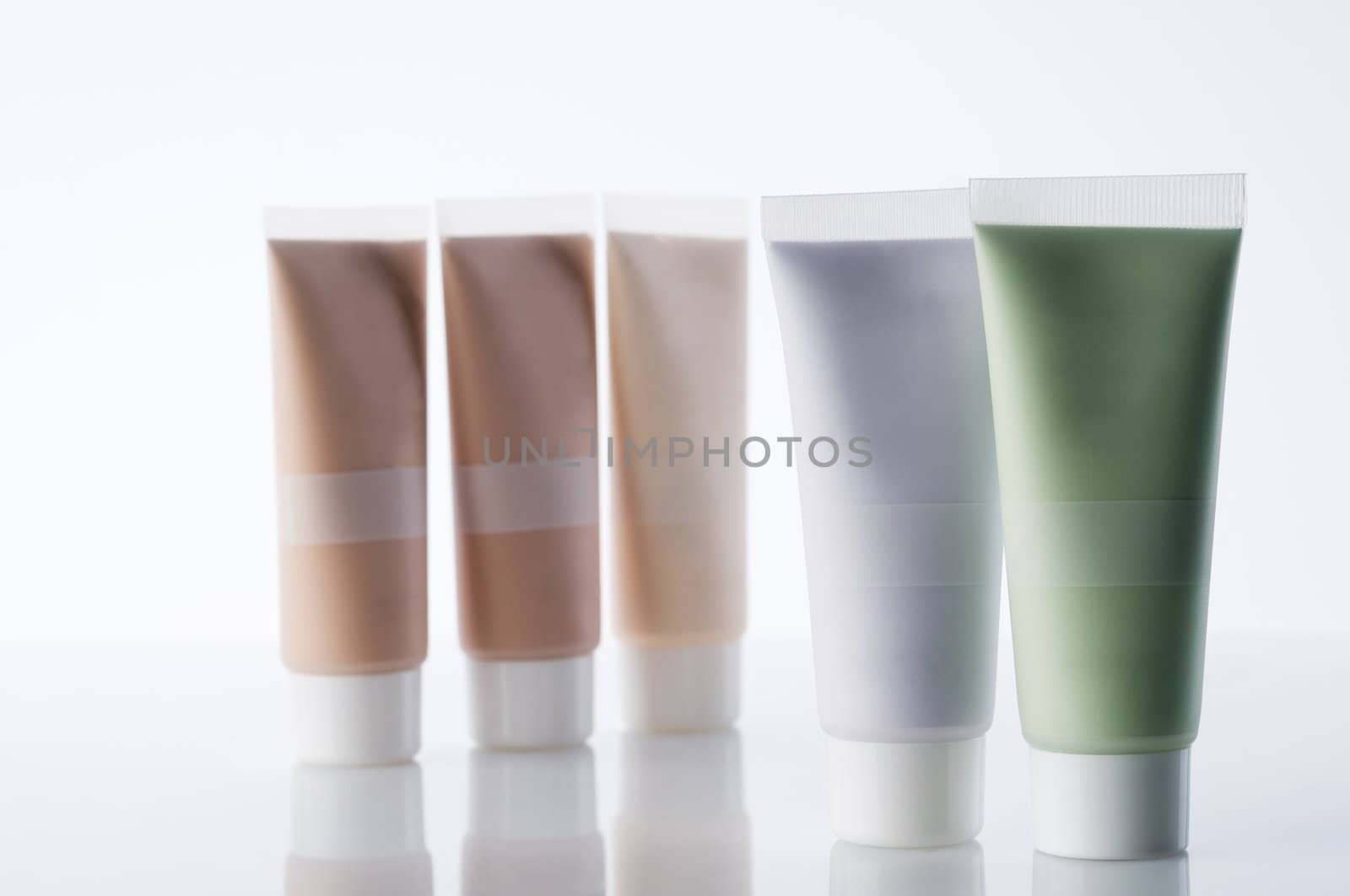Many cosmetic tubes with creams standing on reflective background
