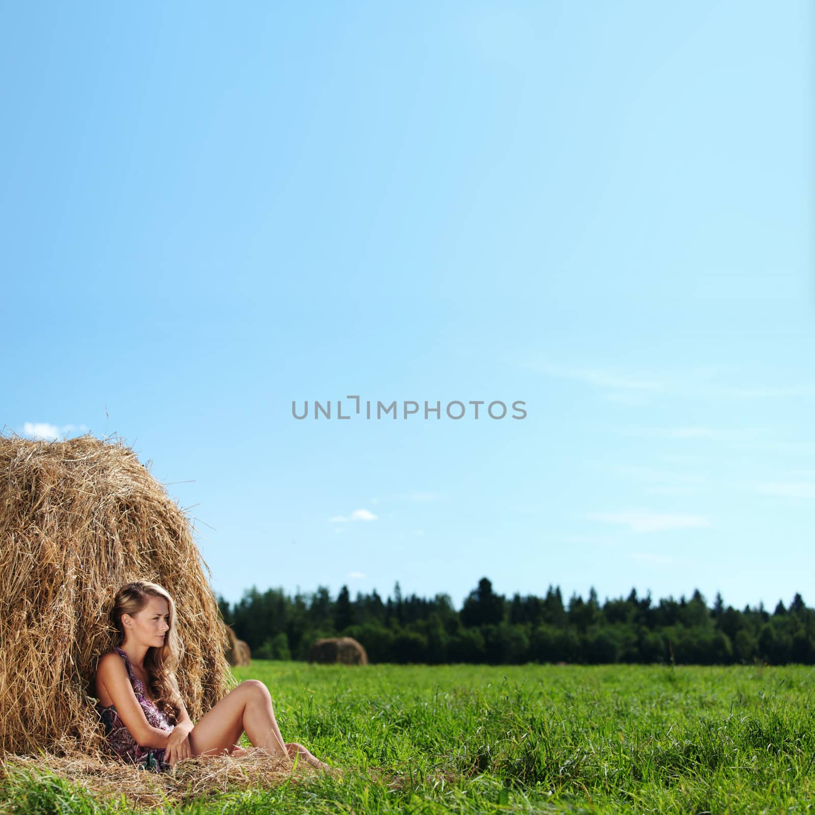 portrait of a girl next to a stack of hay under the blue sky