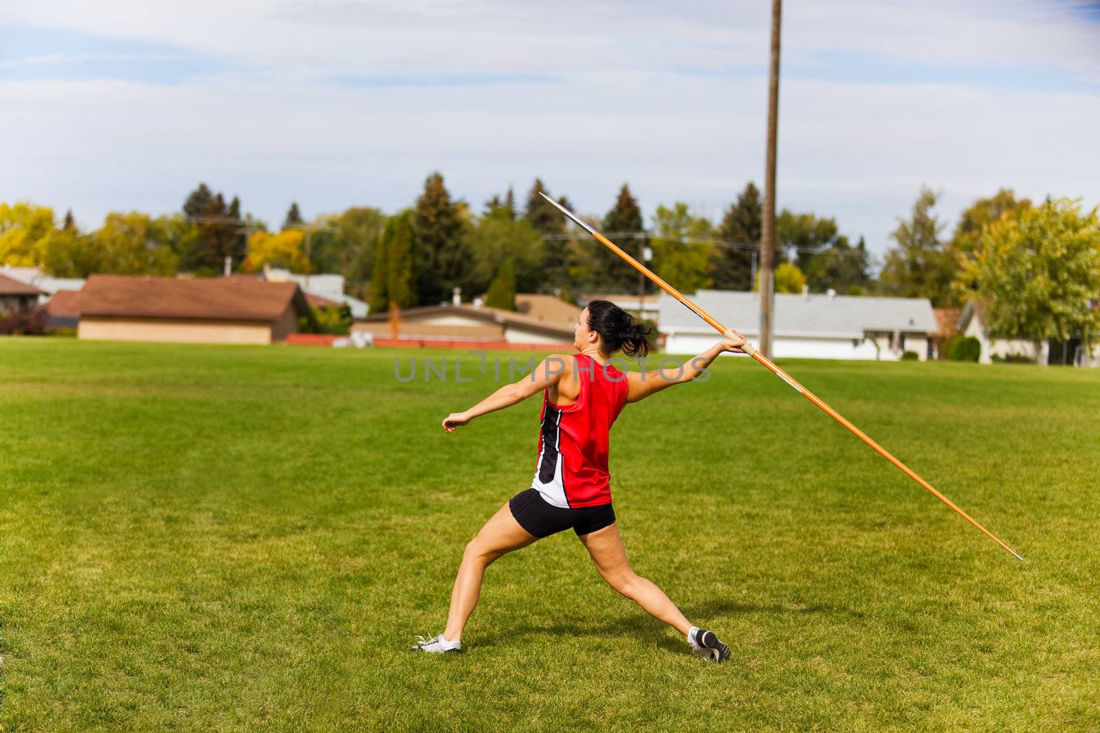 A young, female athlete throwing a javelin in a track and field event.