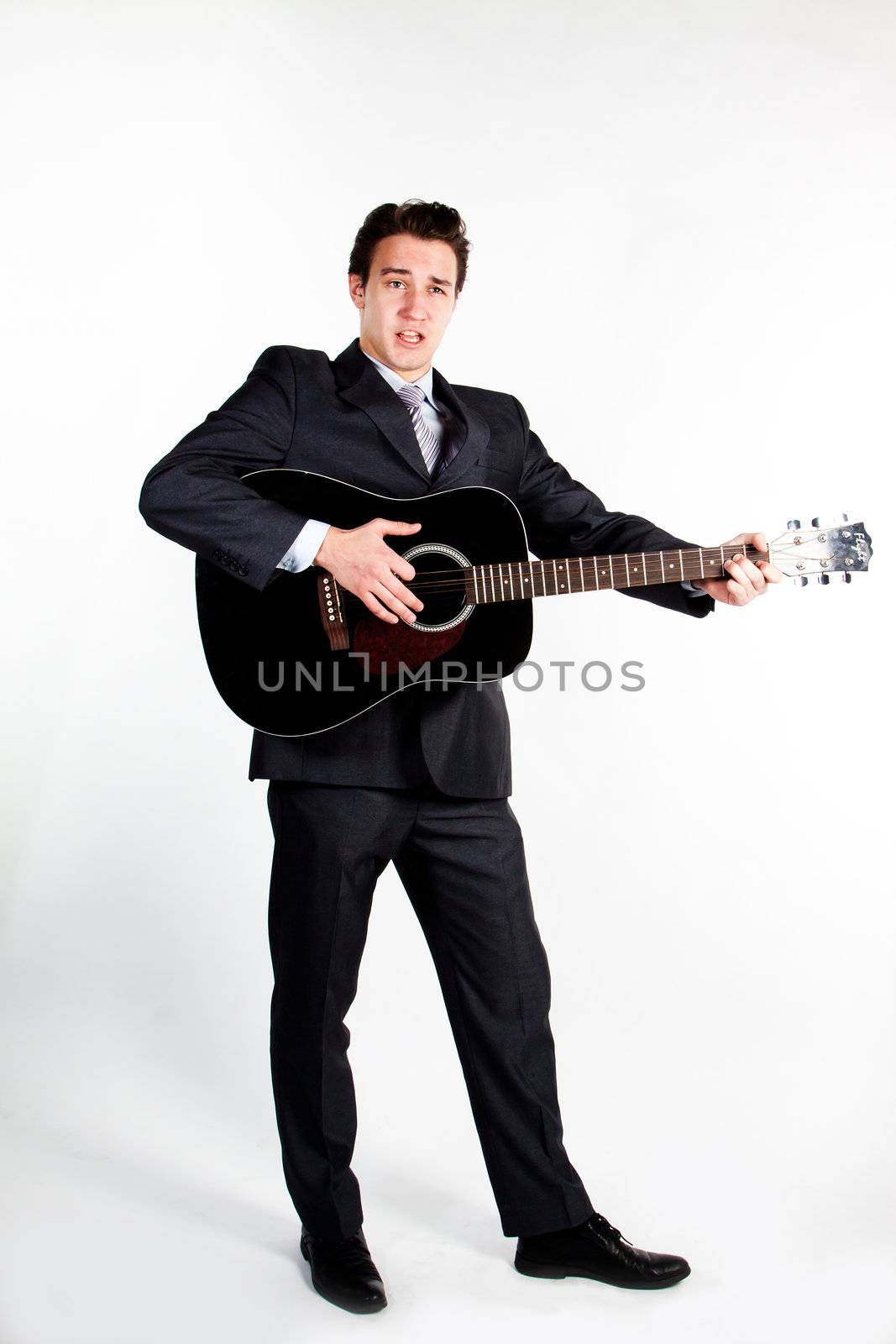 Young handsome man in a dark business suit, sings and plays guitar