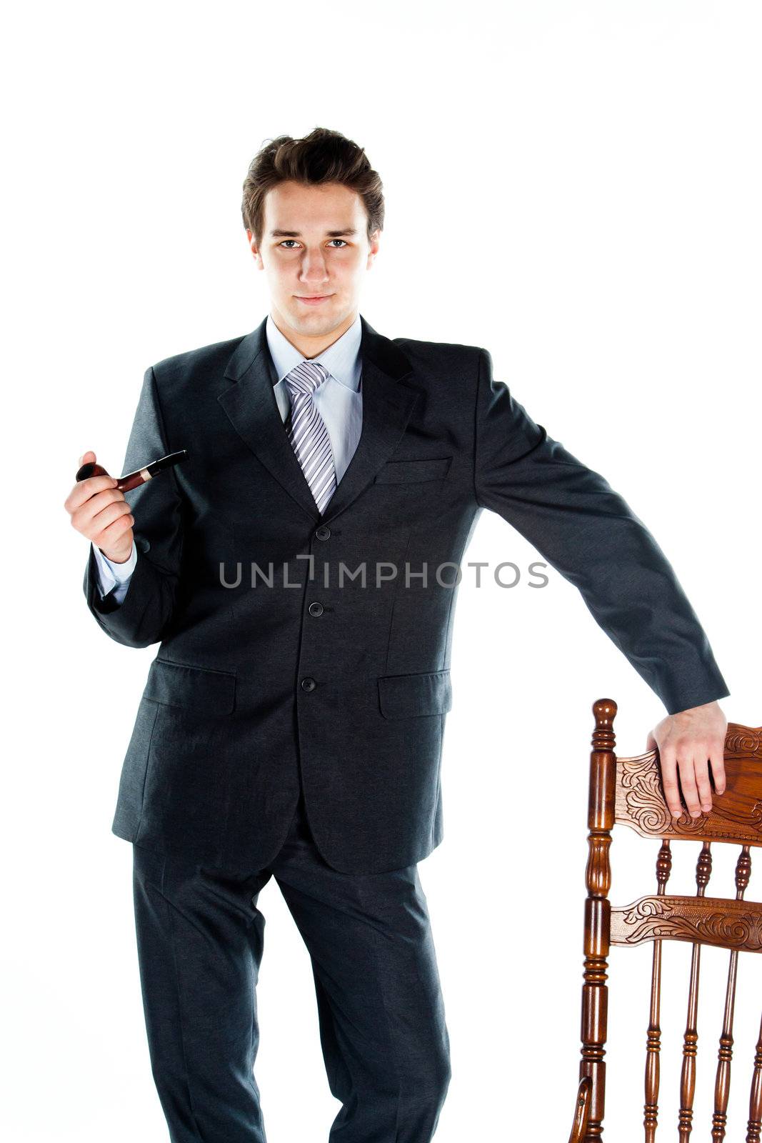 Portrait of a young handsome man in a dark suit with a strict smoking a pipe in his hand