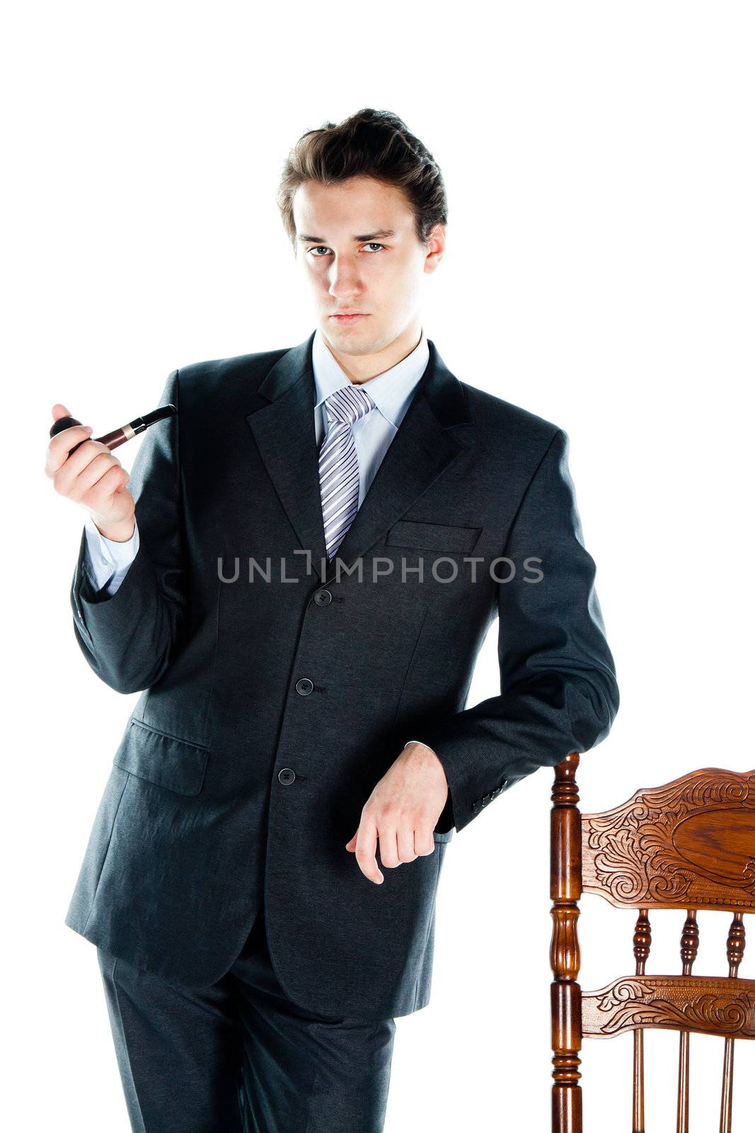 Portrait of a young handsome man in a dark suit with a strict smoking a pipe in his hand