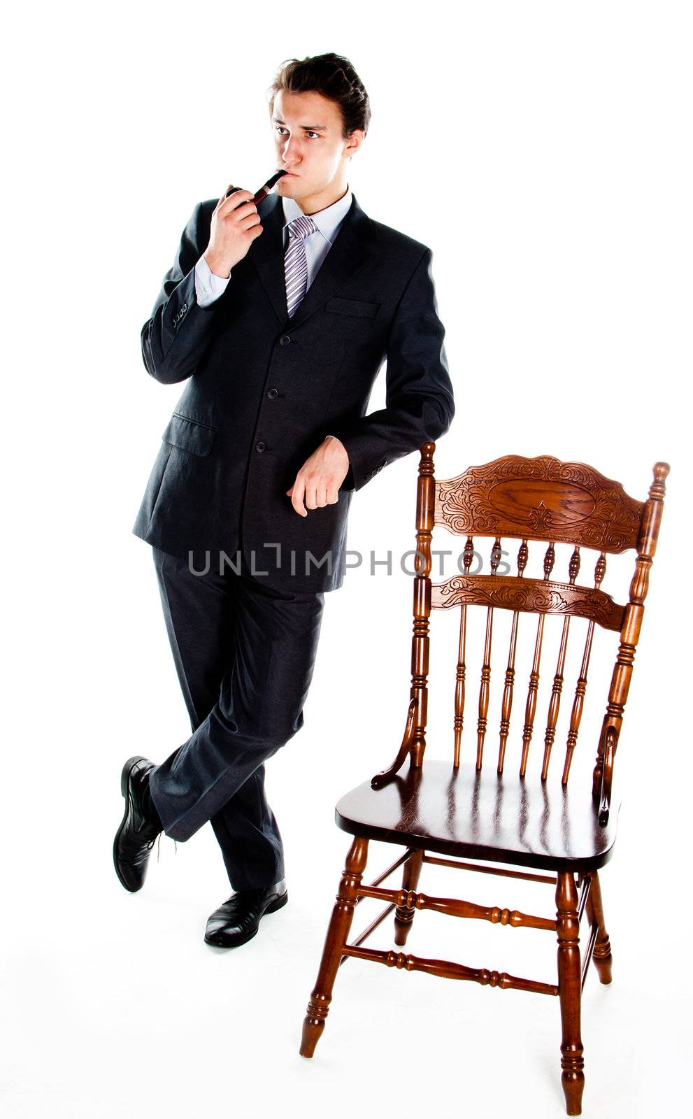 Portrait of a young handsome man in a dark suit with a strict smoking a pipe in his hand