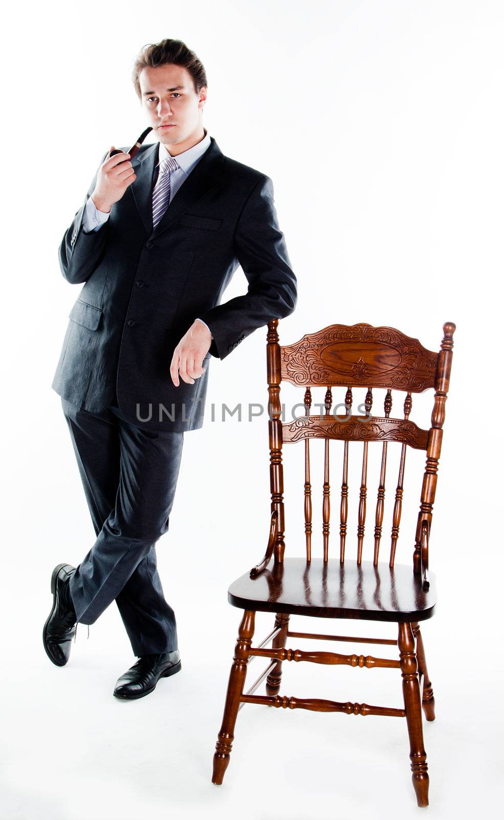 Portrait of a young handsome man in a dark suit with a strict smoking a pipe in his hand