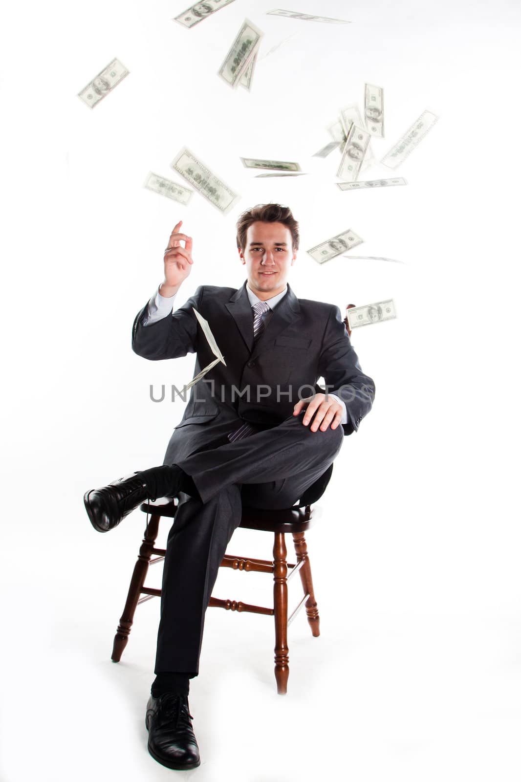 Portrait of a young businessman in a dark suit surrounded by flying dollar bills