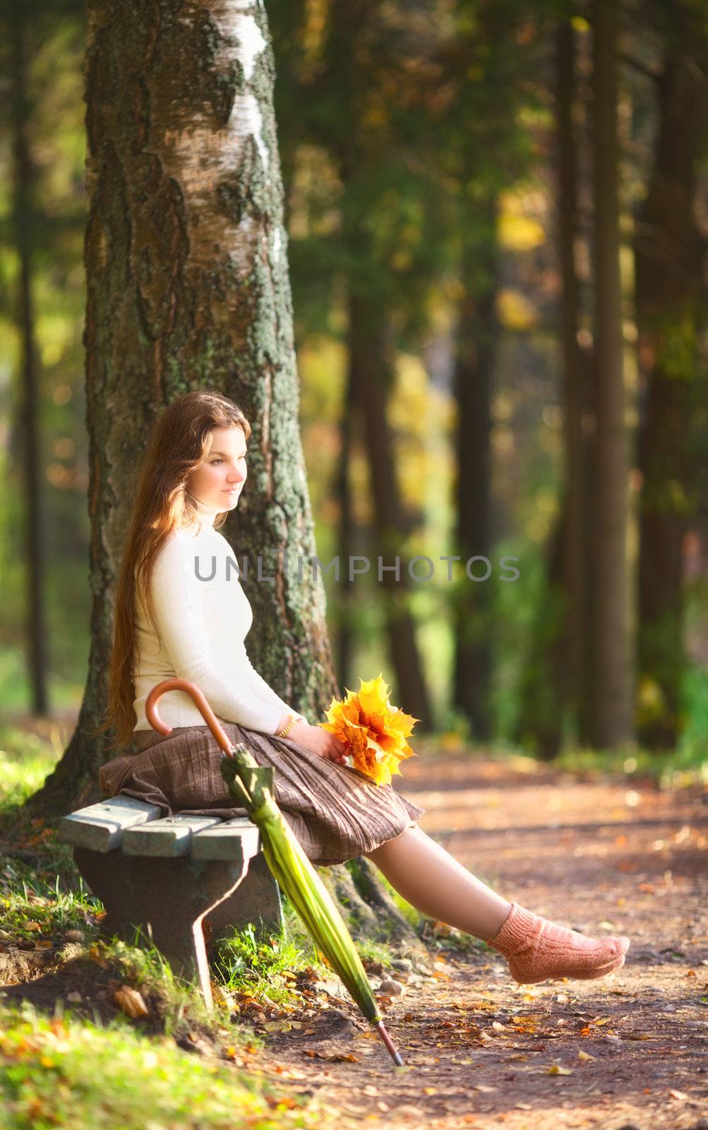 beautiful girl with leaves sitting on bench in autumn park