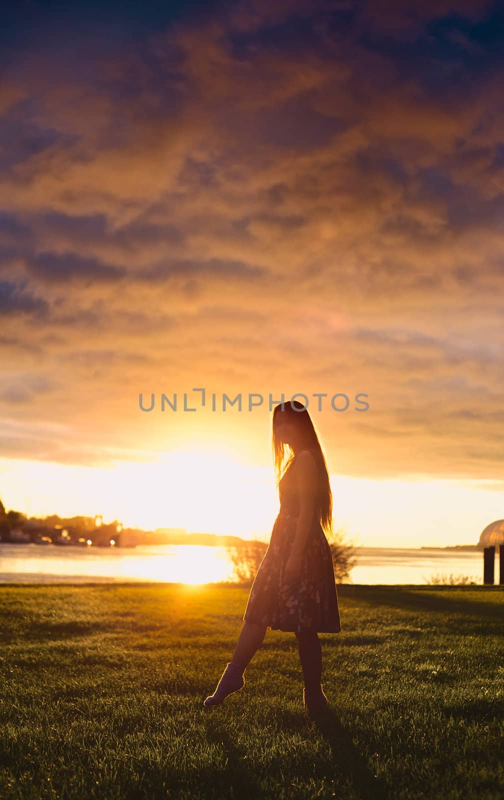 beautiful girl standing on river shore in rays of setting sun