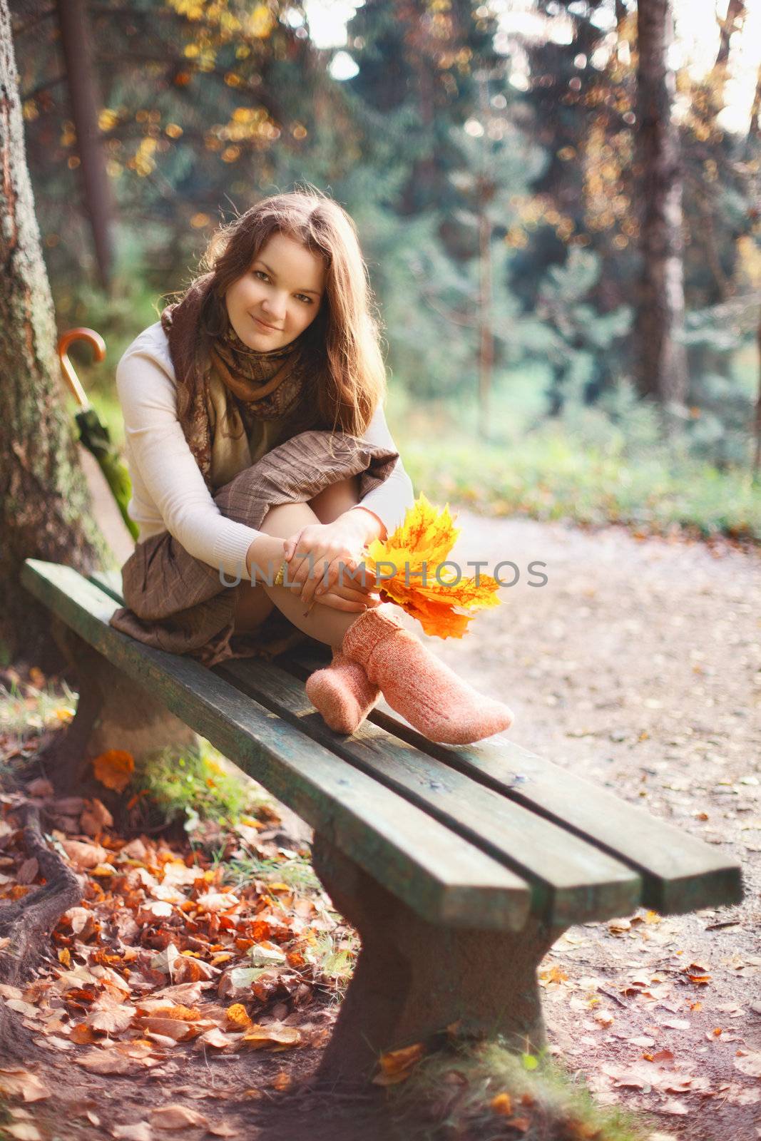 beautiful girl with leaves sitting on bench in autumn park