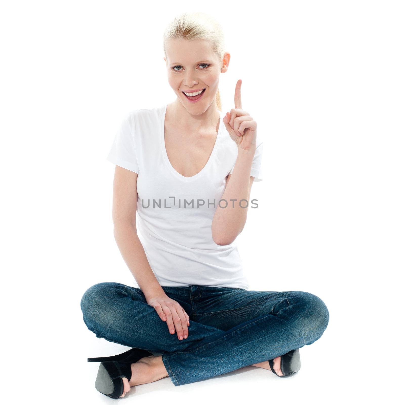 Cute young girl seated on floor and pointing up isolated over white background