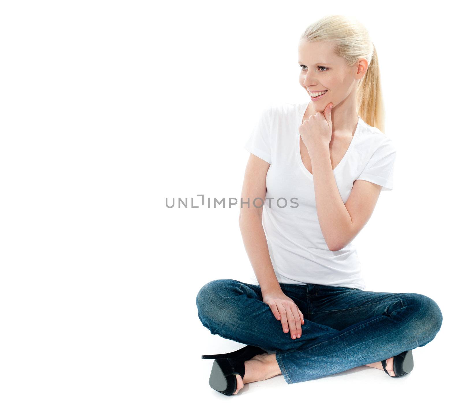 Pretty girl in white top and blue jeans sitting on floor, mischievious smile on face